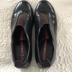 PRADA black loafers with red  accents on the flap.
